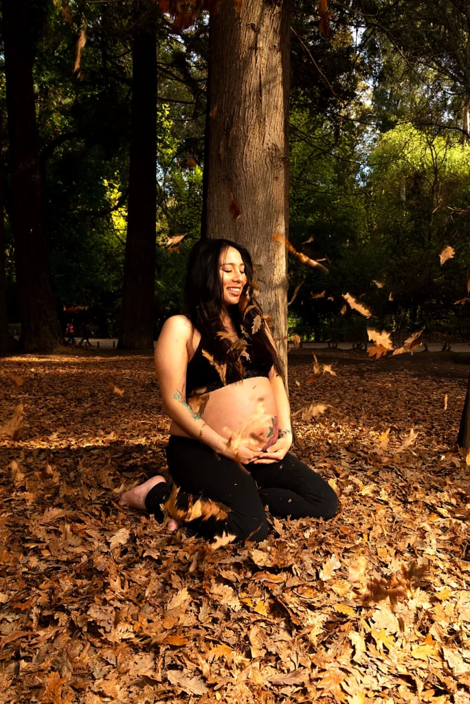 Fotografía en Quilpué: Ideas, Inspiración y Consejos | Arrebol 7 Mujer embarazada con conjunto negro sentada entre hojas de otoño durante una sesión de fotos de maternidad al aire libre.